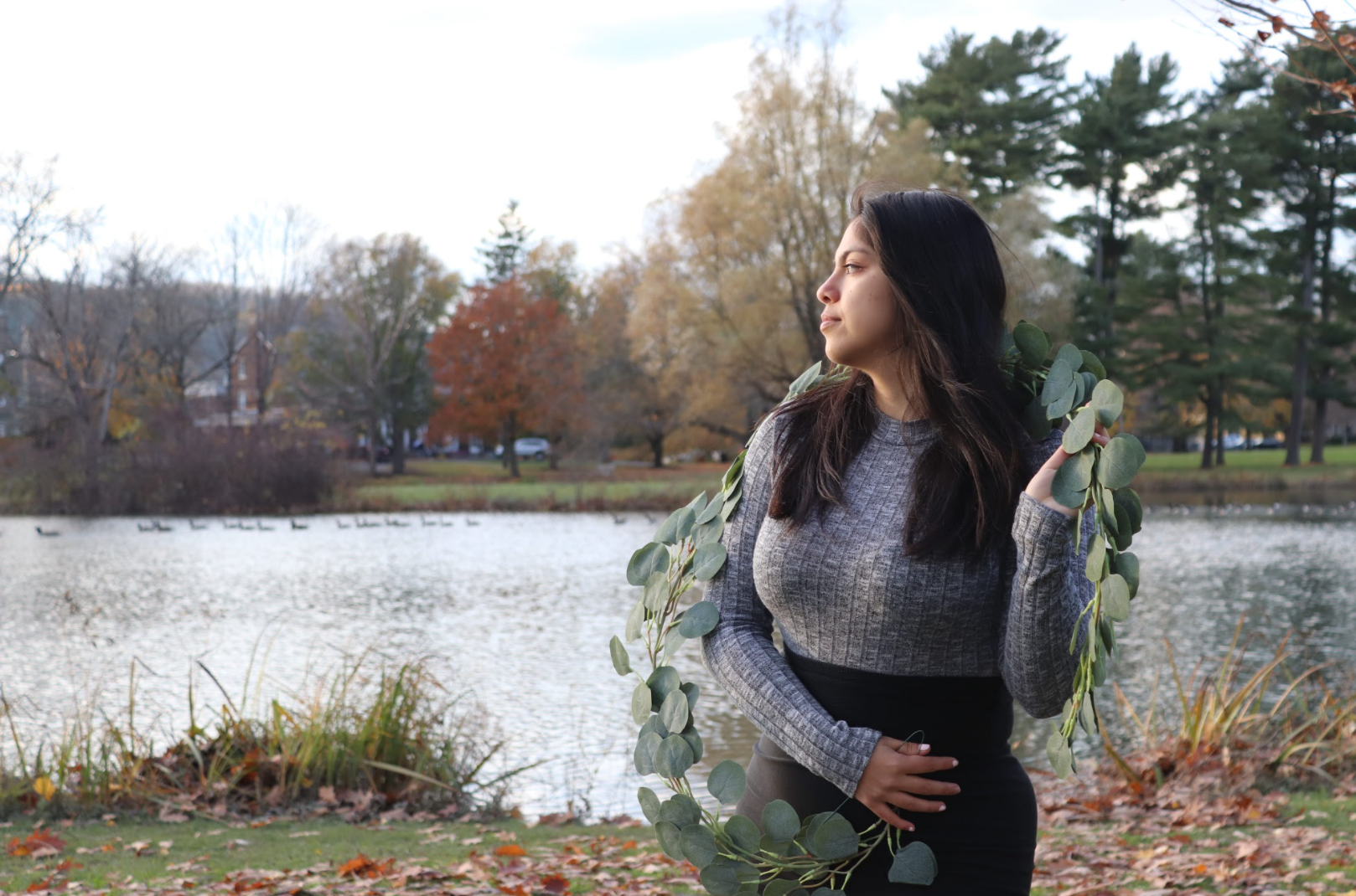 A woman in a grey sustainable sweater is starring at the lake behind her.