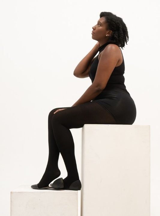 A woman in all black was sitting on the white cube. She was wearing Cloeco's skin-friendly black EverTights.